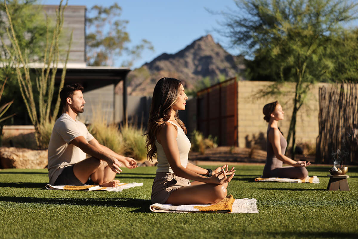 An outdoor green lawn at the Arizona Biltmore Waldorf Resort & Spa. There are several people meditating depicting a relaxing environment.
