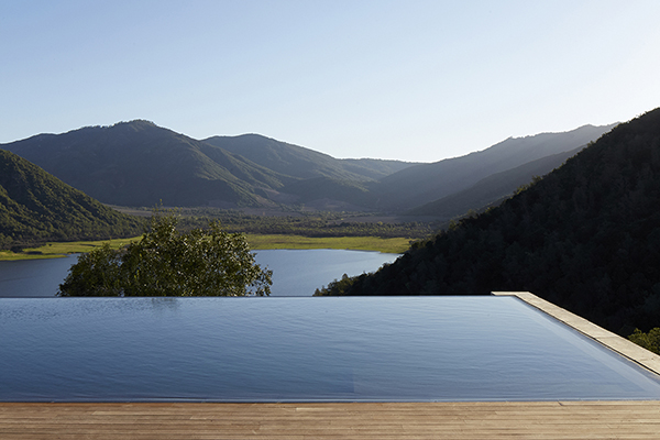 A stunning infinity pool at the VIK Chile hotel, located in the Millahue Valley of Chile. The pool overlooks a picturesque vineyard, surrounded by green hills and mountains in the distance. The image conveys a sense of relaxation and indulgence, with a focus on the natural beauty of Chile and the luxurious spa experience offered at VIK Chile hotel.